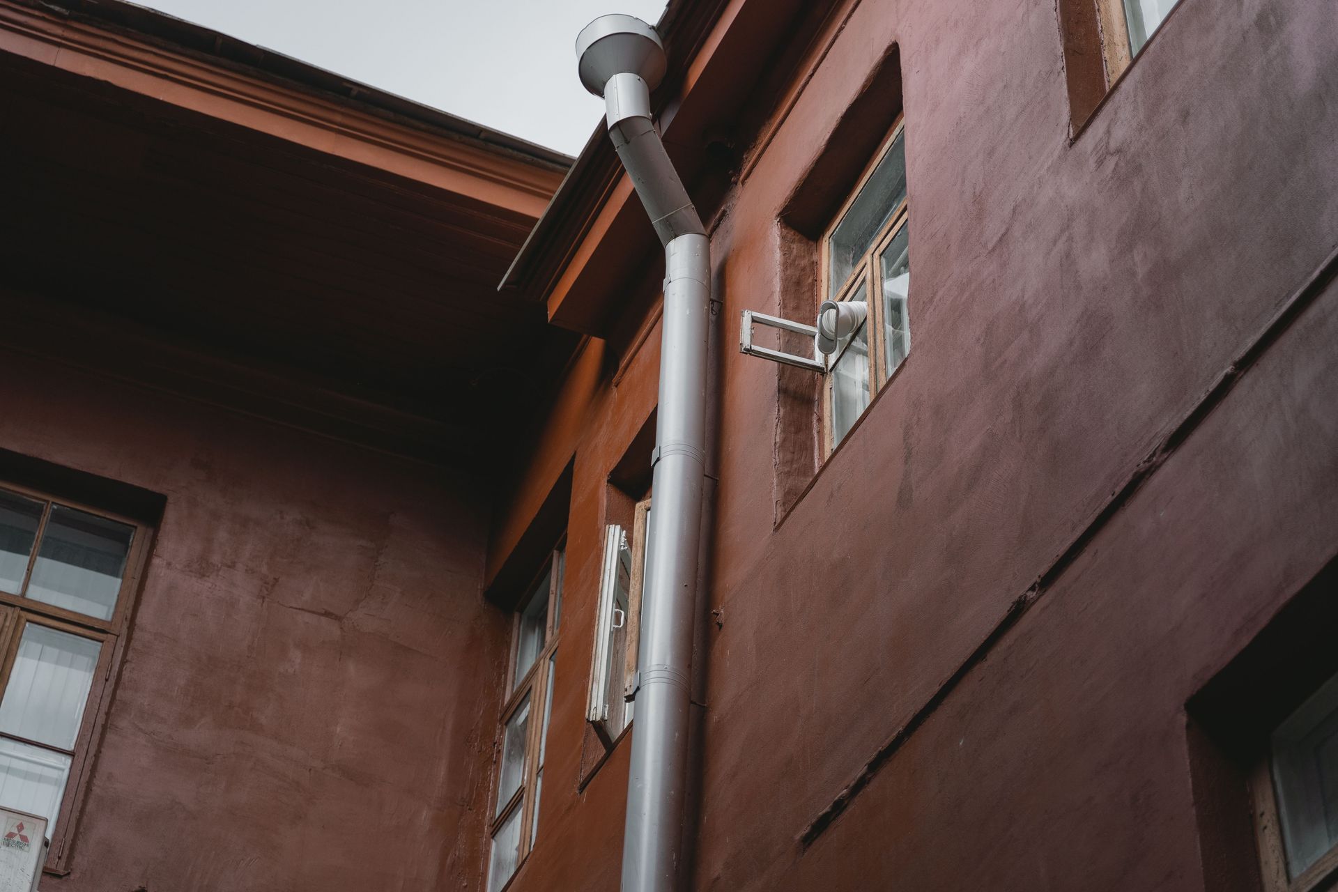 A brown building exterior with pipes and windows, photographed from a low angle.