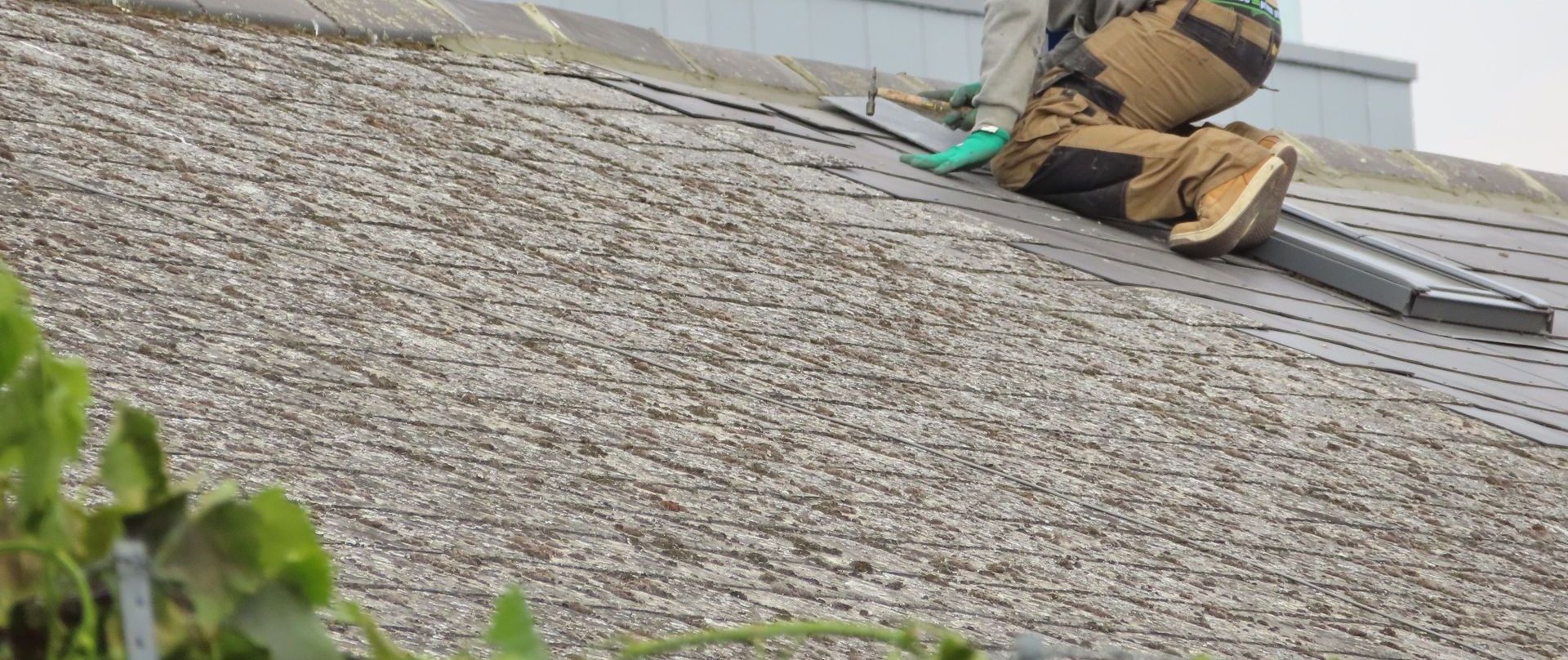 Construction worker installing shingles on a rooftop. Outdoor building maintenance.
