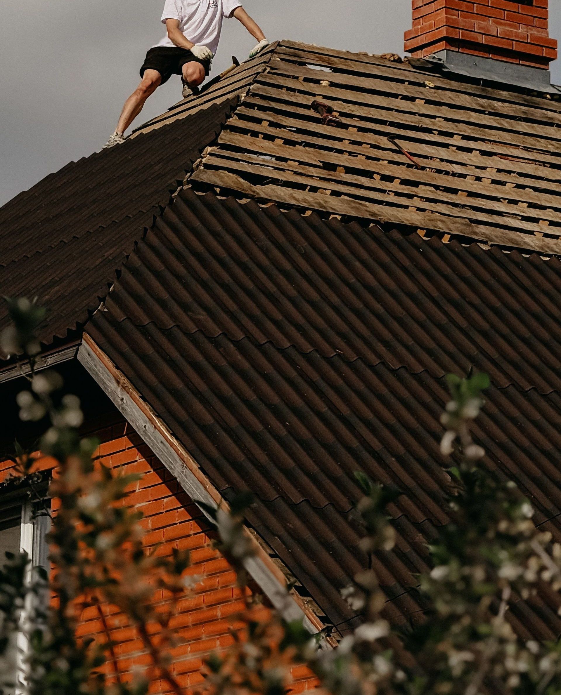 Man in safety helmet repairing roof of red brick house under clear sky.