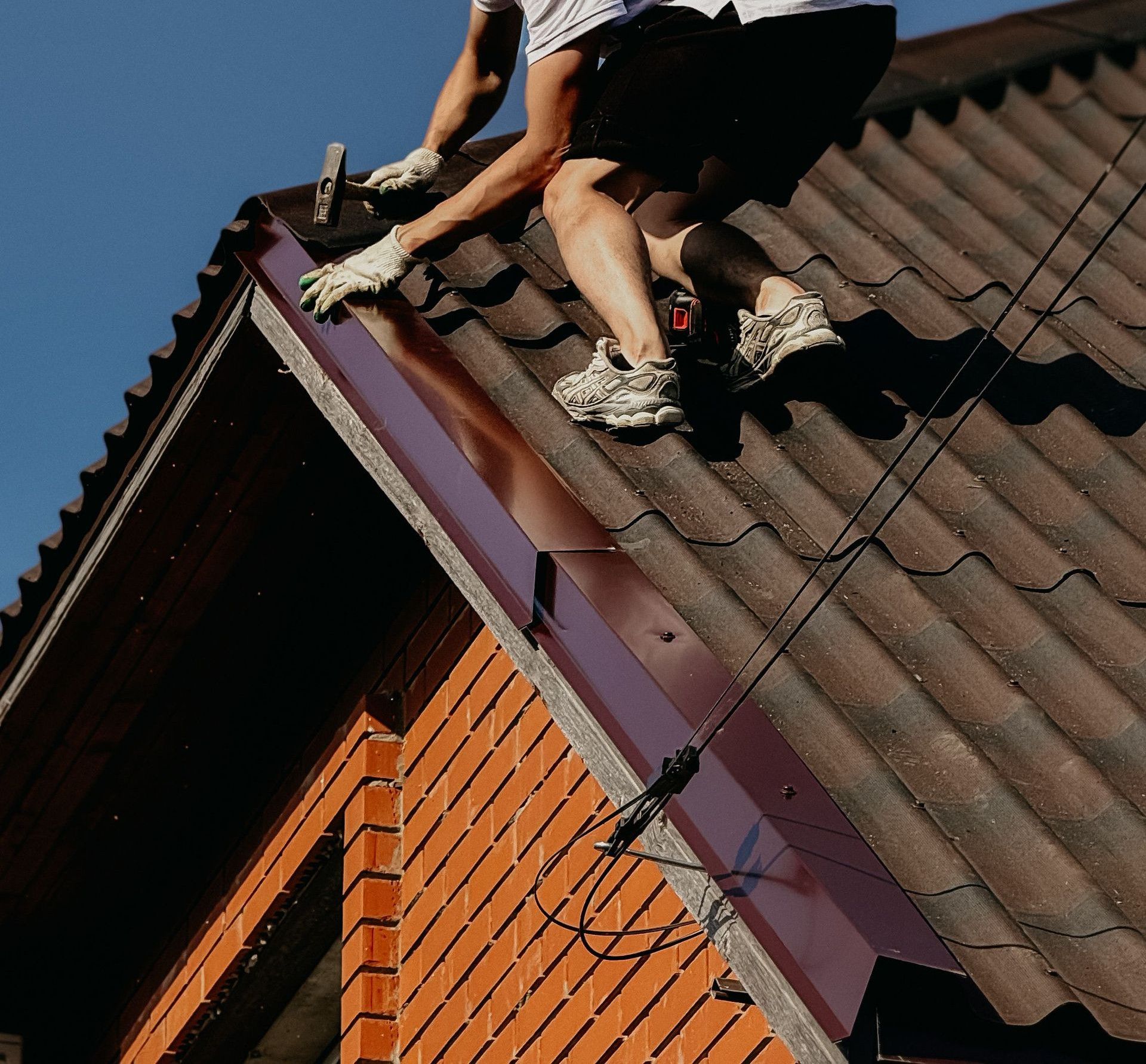 A roofer in a safety helmet renovating a brick house roof under clear blue skies.