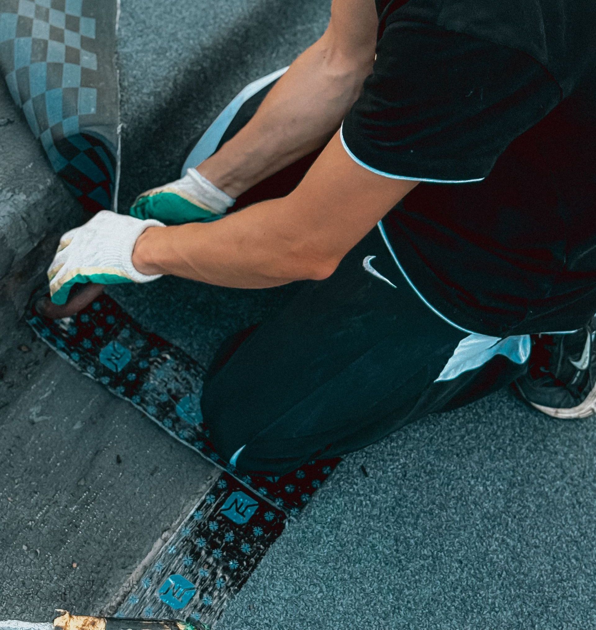 Man wearing gloves and a cap installing shingles on a flat roof on a sunny day.